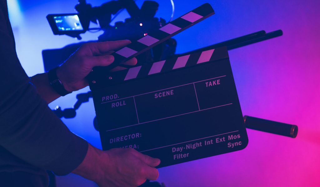 Film Making Professional with Clapperboard in His Hands. Film Production. Studio Interior Illuminated with Red and Blue. Motion Picture Industry Theme.