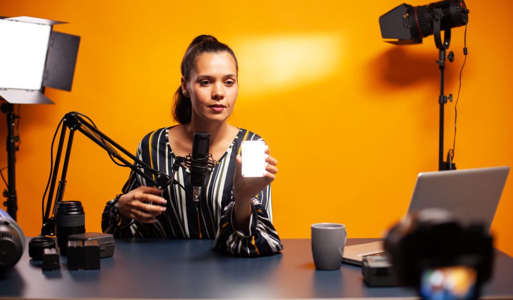 Filmmaker showing mini led light while recording podcast. Video blogger recording a vlog with technology product equipment use in videography and photography.