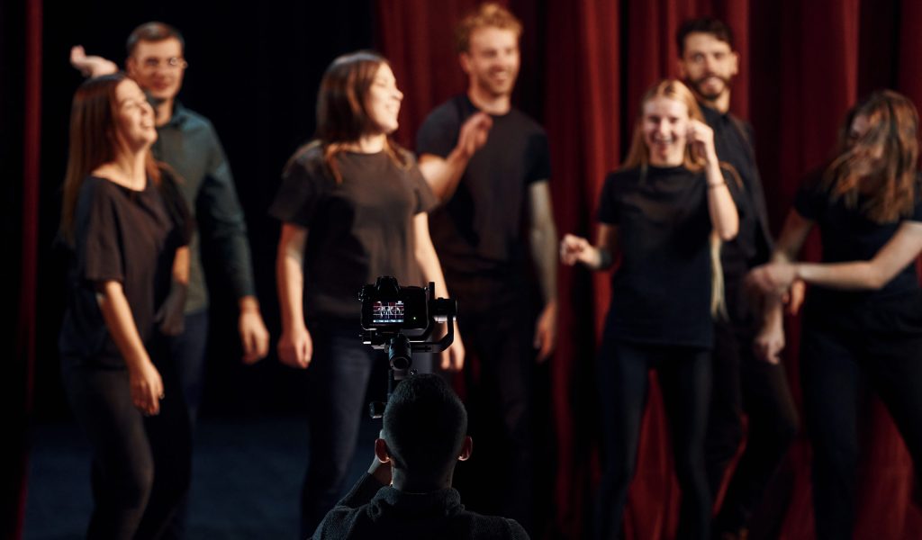 Happy people celebrating success. Group of actors in dark colored clothes on rehearsal in the theater.